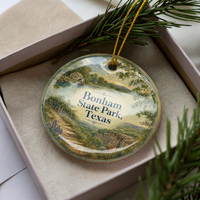 A decorative ornament in a box, featuring a scenic landscape with a path, trees, and a body of water.