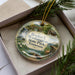 A decorative ornament in a box, featuring a scenic landscape with a river, bridge, and houses, along with the text "Booker T. Washington State Park, Tennessee".