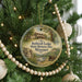 A round ornament hanging on a Christmas tree, featuring a scenic image of a historic lodge surrounded by trees and a stream.