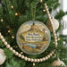 A round ornament hanging on a Christmas tree, featuring a scenic landscape with a mountain, windmill, and deer.