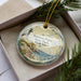 A decorative ornament in a box, featuring a lighthouse and a coastal scene, with the text "Brenton Point State Park, Rhode Island" on it.