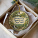 A round ornament with a scenic image of a park, featuring a bridge, trees, and a waterfall, is displayed in a box.