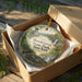 A round ornament in a box, featuring a scenic landscape with a castle, trees, and a waterfall, with the text "Brookhaven State Park, New York" prominently displayed.