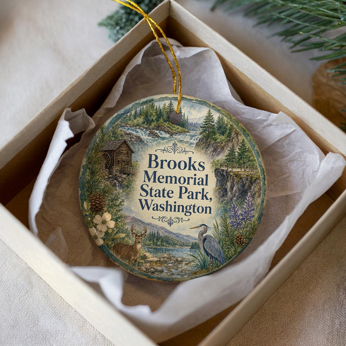 A decorative ornament in a white box, featuring a scenic landscape with a river, trees, and wildlife.