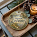 A wooden tray with a decorative ornament featuring a scenic landscape, pine cones, and a lit candle.