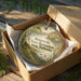 A round ornament in a brown box, featuring a scenic landscape with a lake, trees, and birds, along with the text "Brownville State Recreation Area, Nebraska".