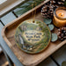 A decorative ornament featuring a scenic image of the scenic overlook at Bryant Creek State Park in Missouri, with pine cones and a lit candle on a wooden tray.