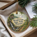 A decorative ornament with a scenic image of a waterfall and a house, surrounded by greenery, placed in a box.