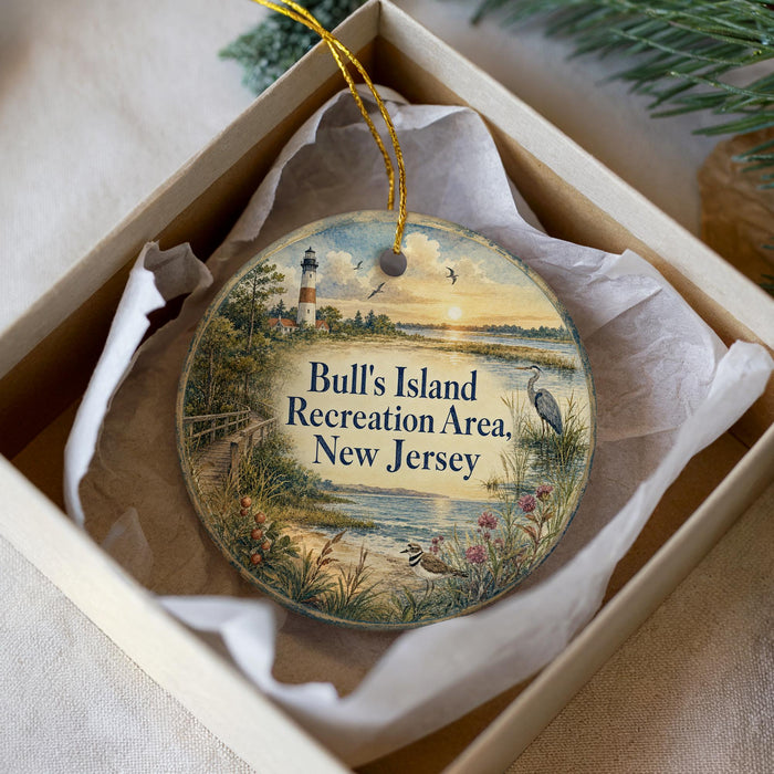 A decorative ornament in a box, featuring a lighthouse and a scenic landscape with a body of water and birds.