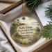 A decorative ornament with a lighthouse and a scenic landscape, placed in a box with pine branches.