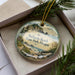 A decorative ornament with a scenic image of Bullards Beach, Oregon, displayed in a box with pine branches.