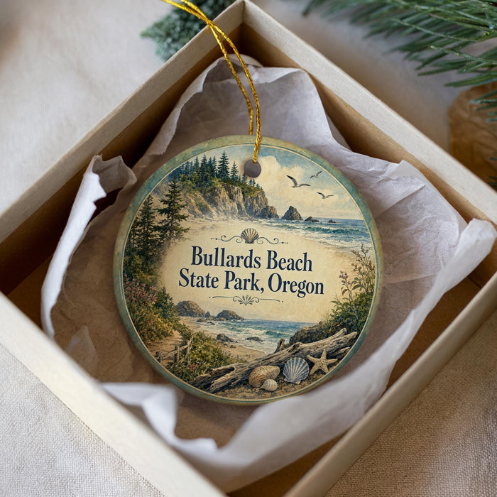 A circular ornament with a scenic beach landscape and text, placed in a box with a white tissue paper lining.