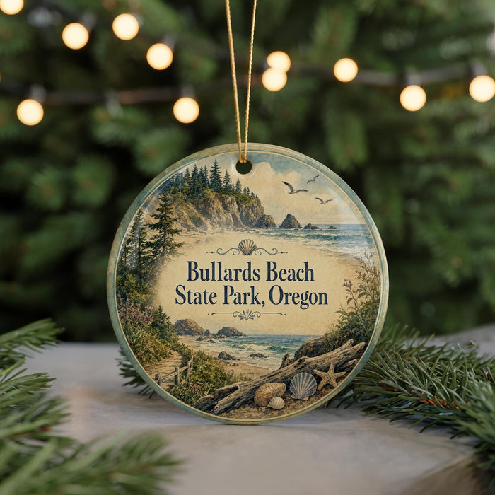 A circular ornament with a scenic beach landscape and text that reads "Bullards Beach State Park, Oregon" is displayed in front of a blurred background of Christmas lights.