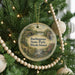 A round ornament hanging on a Christmas tree, featuring a scenic landscape with a bridge and water.
