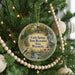 A round ornament hanging on a Christmas tree, featuring a scenic landscape with a bird and a house.