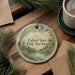 A round ornament with a scenic landscape of Calvert Vaux Park, New York, hangs on a wooden surface.