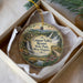 A decorative ornament in a white box, featuring a scenic landscape with a waterfall, trees, and a path leading to a resort.