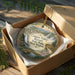 A decorative ornament in a wooden box, featuring a scenic landscape with a waterfall and mountains, with the text "Canaan Valley Resort State Park, West Virginia" printed on it.