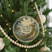 A round ornament hanging on a Christmas tree, featuring a lighthouse and a coastal landscape.