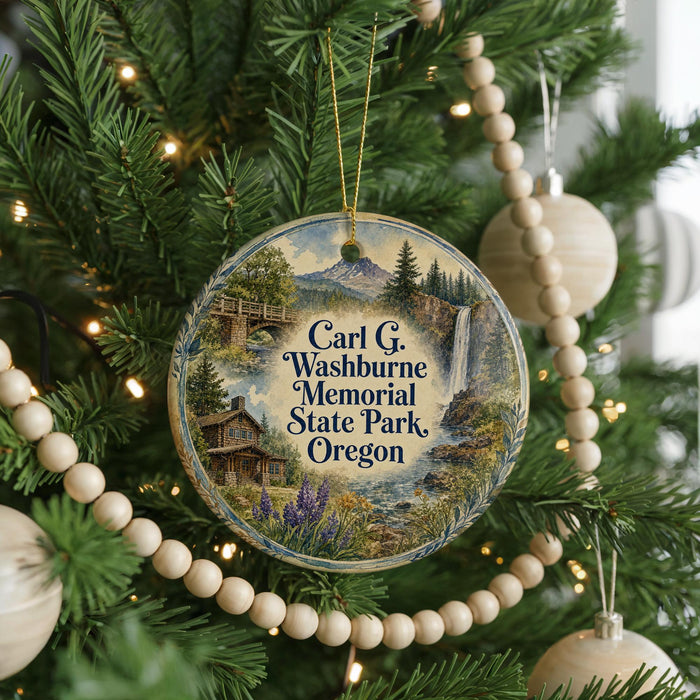 A round ornament hanging on a Christmas tree, featuring a scenic landscape with a waterfall and a cabin.