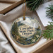 A decorative ornament with the text "Cascadia State Park, Oregon" printed on it, hanging from a string. The ornament is placed inside a box with pine branches and greenery, creating a natural and festive atmosphere.