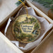 A decorative ornament in a box, featuring a scenic landscape with a bridge, trees, and a waterfall.
