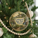 A round ornament hanging on a Christmas tree, featuring a scenic landscape with a bridge and waterfalls.