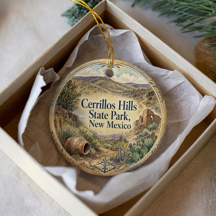 A decorative ornament in a box, featuring a scenic landscape with mountains, cacti, and a barrel, with the text "Cerrillos Hills State Park, New Mexico" printed on it.
