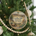 A round ornament hanging on a Christmas tree, featuring a scenic landscape of hills and a desert.
