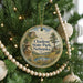 A round ornament hanging on a Christmas tree, featuring a scenic landscape with a mountain and a lake.