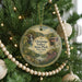 A round ornament hanging on a Christmas tree, featuring a scenic landscape with a waterfall and a bridge.