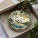 A decorative ornament with a scenic image of Clayton Lake State Park, Oklahoma, displayed in a box with pine branches.