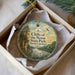 A round ornament with a scenic landscape of cliffs, trees, and a river, hanging from a string.