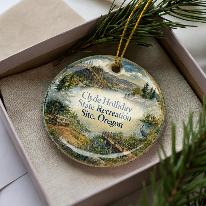 A decorative ornament in a box, featuring a scenic landscape with mountains, trees, and a body of water.