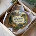 A round ornament with a scenic landscape, featuring a lake, mountains, and a bird, is displayed in a box.