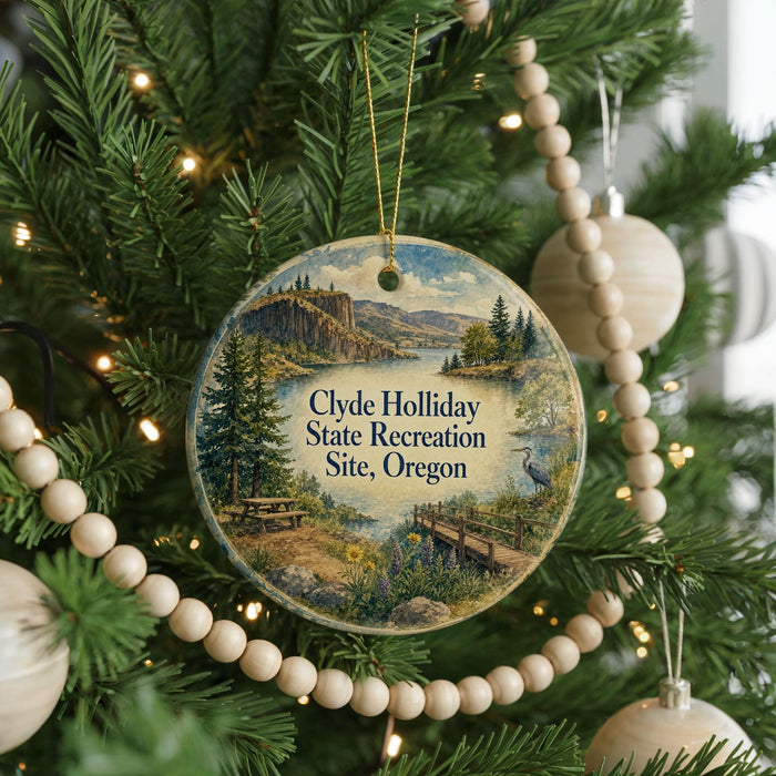 A round ornament hanging on a Christmas tree, featuring a scenic landscape with a lake, mountains, and trees.