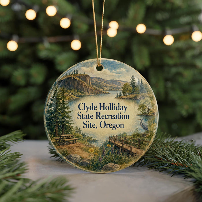 A round ornament with a scenic landscape featuring a lake, mountains, and a bridge, hanging from a string.