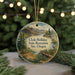 A round ornament with a scenic landscape featuring a lake, mountains, and a bridge, hanging from a string.