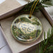 A decorative ornament in a box, featuring a scenic landscape with a bridge and trees, with the text "Coles Creek State Park New York" prominently displayed.