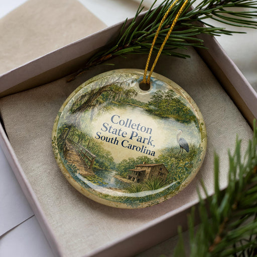 A decorative ornament in a box, featuring a scenic landscape with a bird and a house, surrounded by greenery.