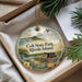 A decorative ornament with a scenic image of a park, featuring a castle, sailboat, and other natural elements, is displayed in a box with pine branches.