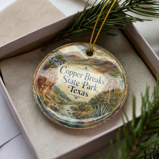 A decorative ornament in a box, featuring a scenic landscape with mountains, trees, and a river.