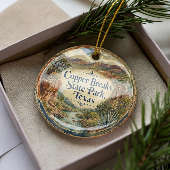 A decorative ornament in a box, featuring a scenic landscape with mountains, trees, and a river.