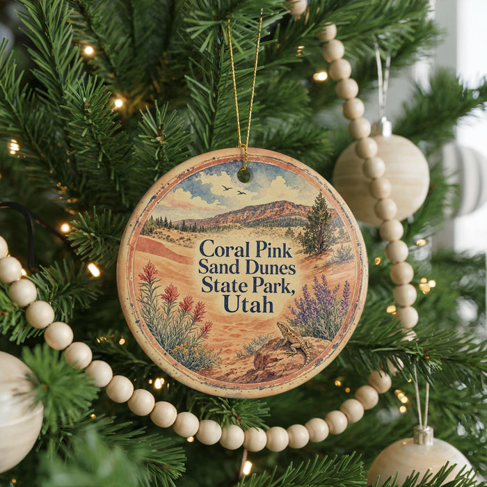 A round ornament hanging on a Christmas tree, featuring a scenic image of the Corall Pink Sand Dunes State Park in Utah.