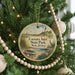 A round ornament hanging on a Christmas tree, featuring a lighthouse and a boat on a beach.