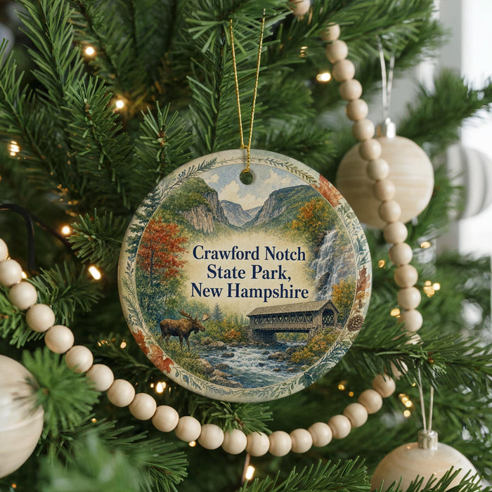 A round ornament hanging on a Christmas tree, featuring a scenic image of a bridge and mountains in New Hampshire.