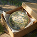 A decorative ornament in a brown box, featuring a scenic landscape with a waterfall and trees, with the text "Croft State Park, South Carolina" printed on it.