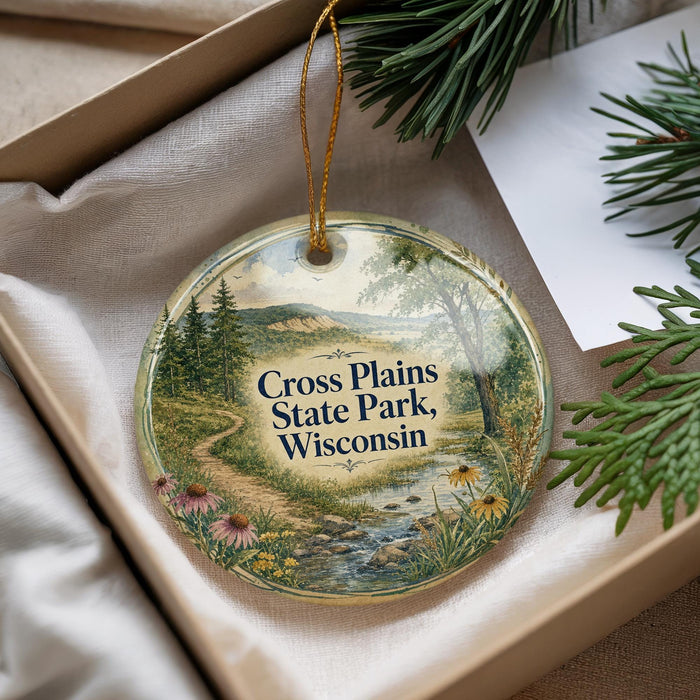 A decorative ornament with a scenic landscape of Cross Plains State Park, Wisconsin, featuring a winding path, pine trees, and a river.