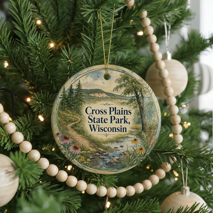 A round ornament hanging on a Christmas tree, featuring a scenic landscape with a river and mountains.