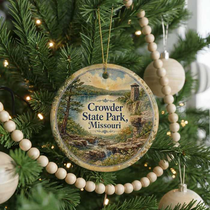 A round ornament hanging on a Christmas tree, featuring a scenic landscape with a waterfall and a tower.